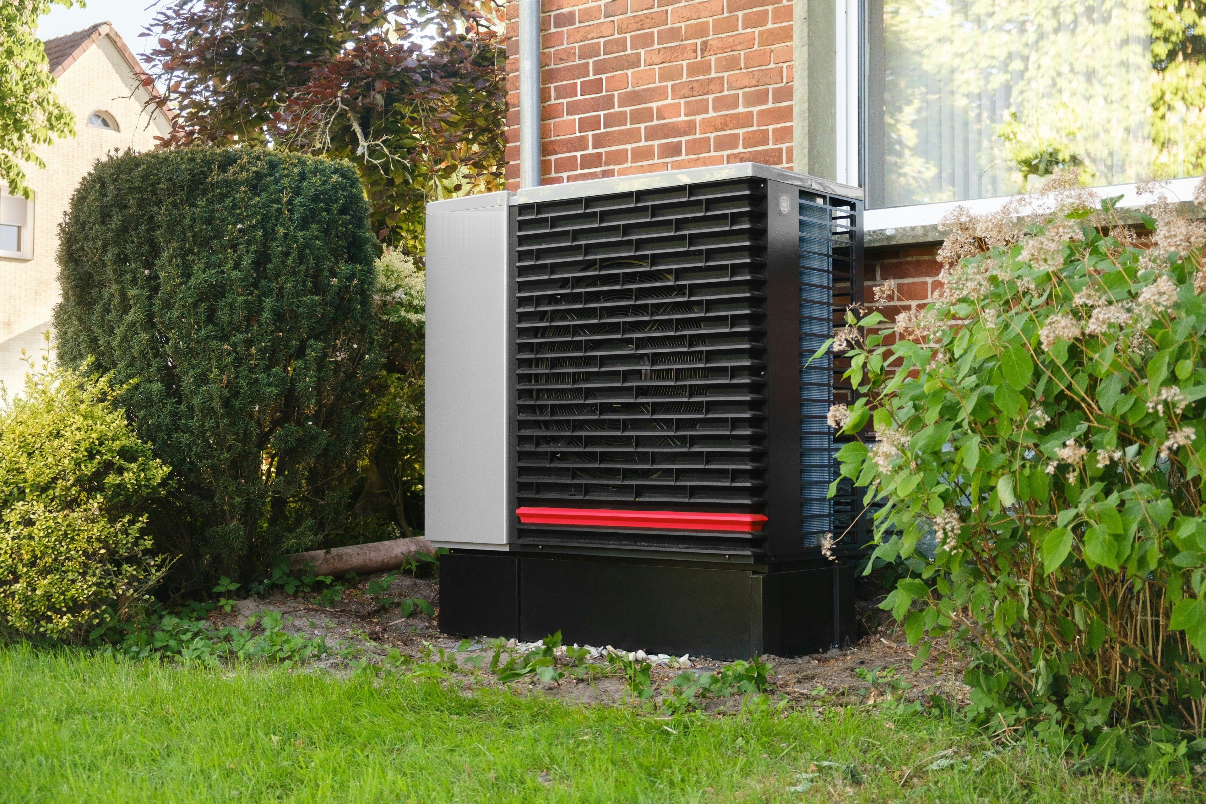 Stock photo of an outdoor air source heat pump unit beside a brick house, shown for illustration