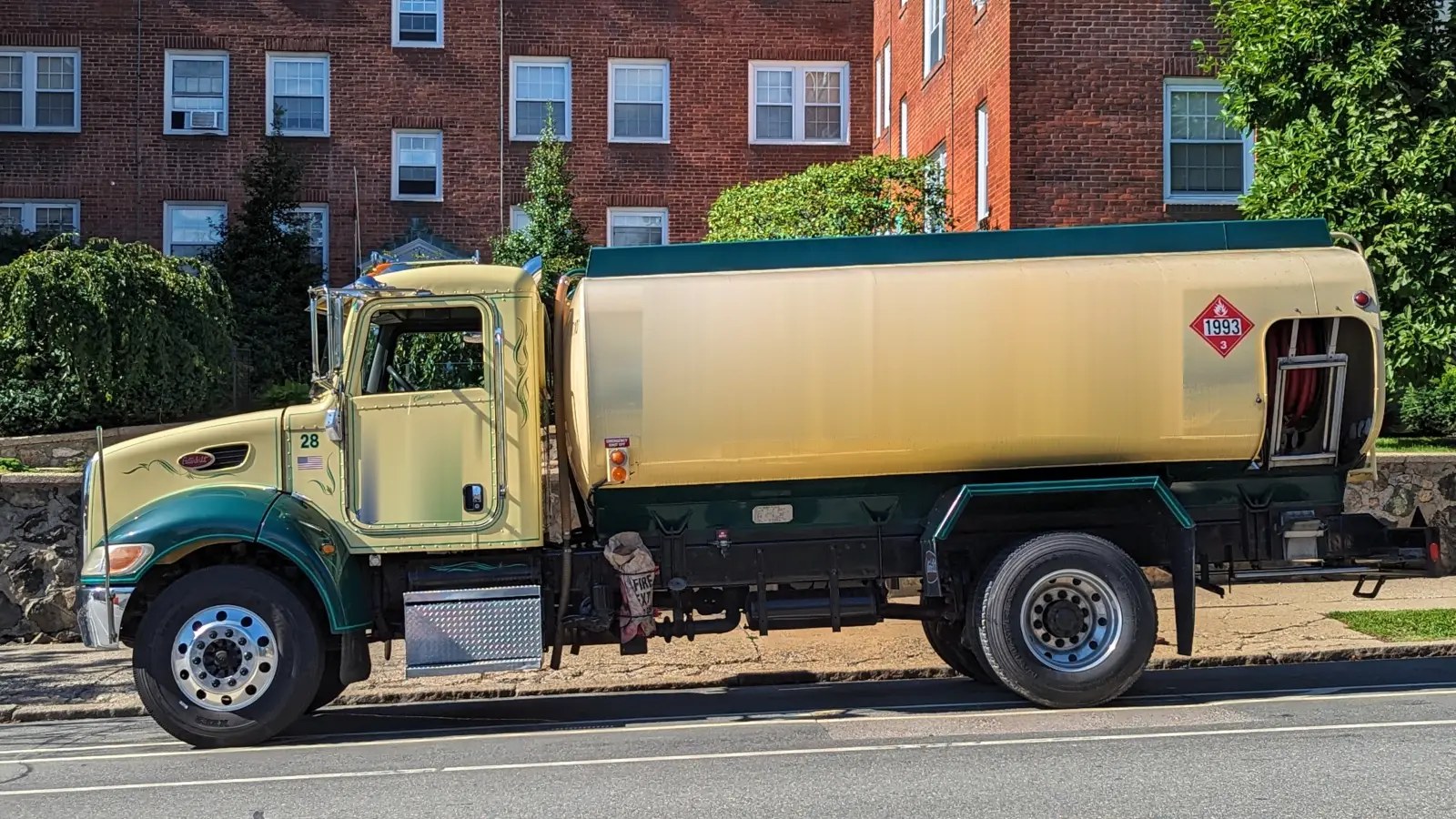 Photo of a heating oil delivery truck with a cream tank and green trim parked on a residential street, company lettering removed, shown for illustration