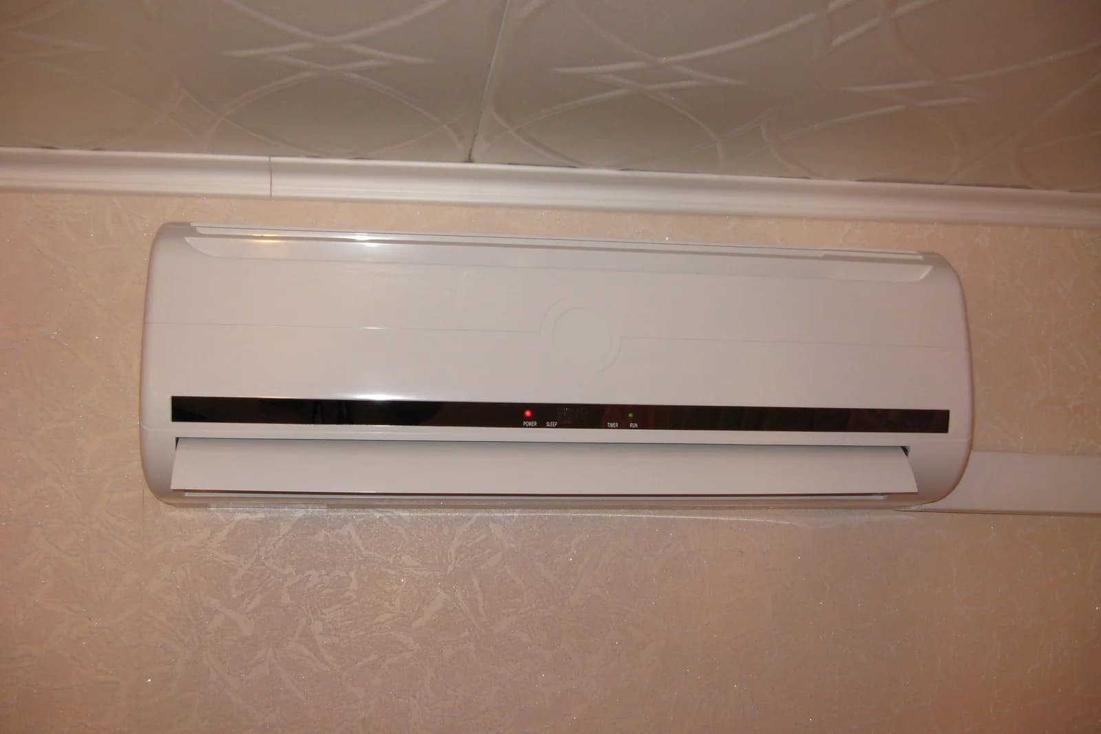Photo of a white wall-mounted mini-split indoor head installed high on an interior wall below the ceiling trim, shown for illustration